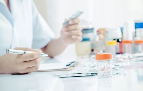 A person sitting at a table with some pills and a cell phone.