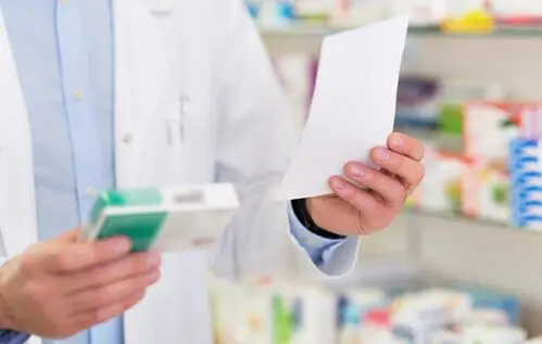 A pharmacist holding a box of pills and papers.